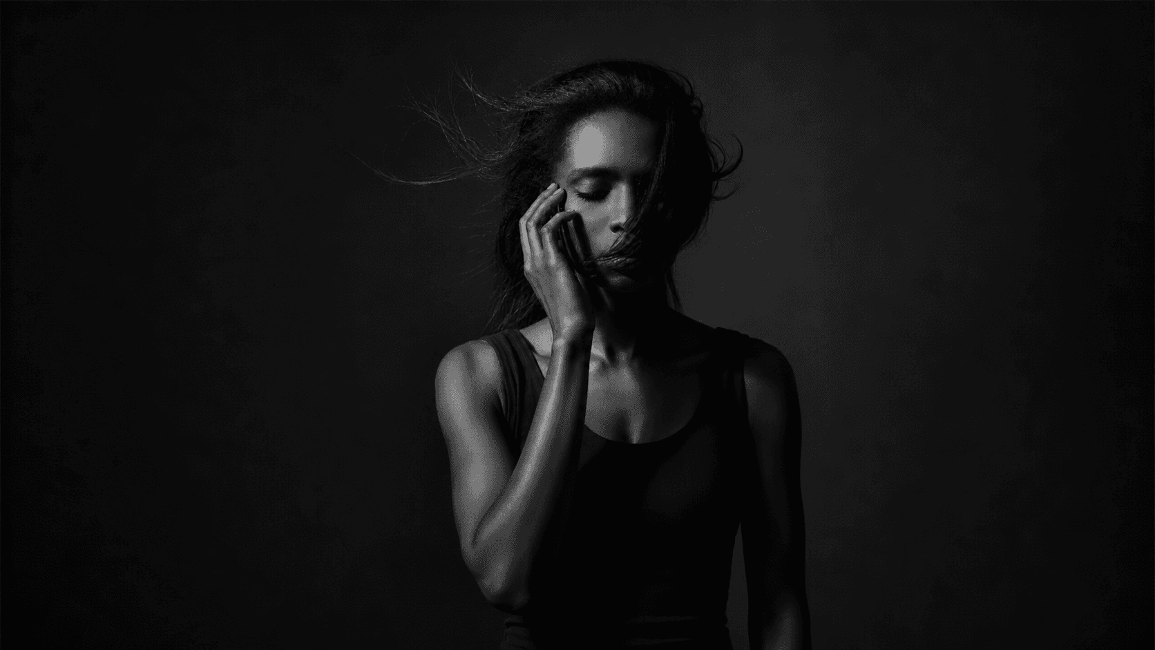 A woman alone in dim light with her eyes closed, sitting with the question of whether infidelity is a dealbreaker.