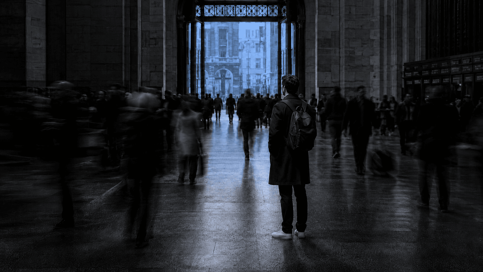 Man standing motionless in a blurred, moving crowd, illustrating the isolation emotional support is meant to address