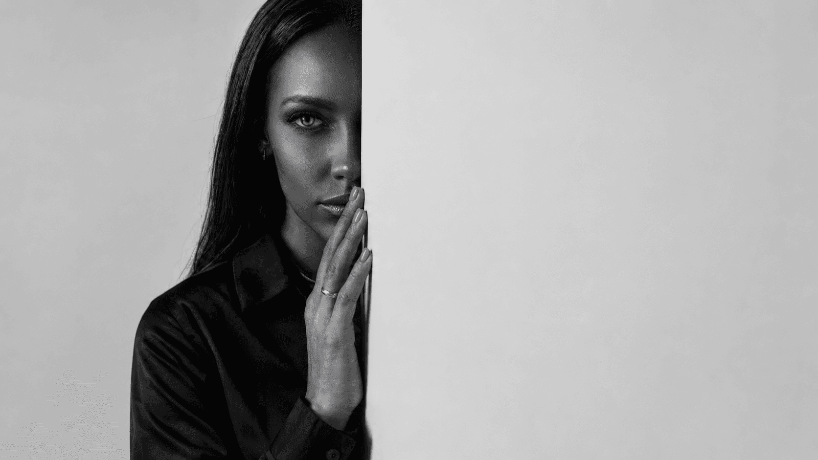 Woman half-hidden behind a wall weighing reconciliation after infidelity, hand raised to her lips.