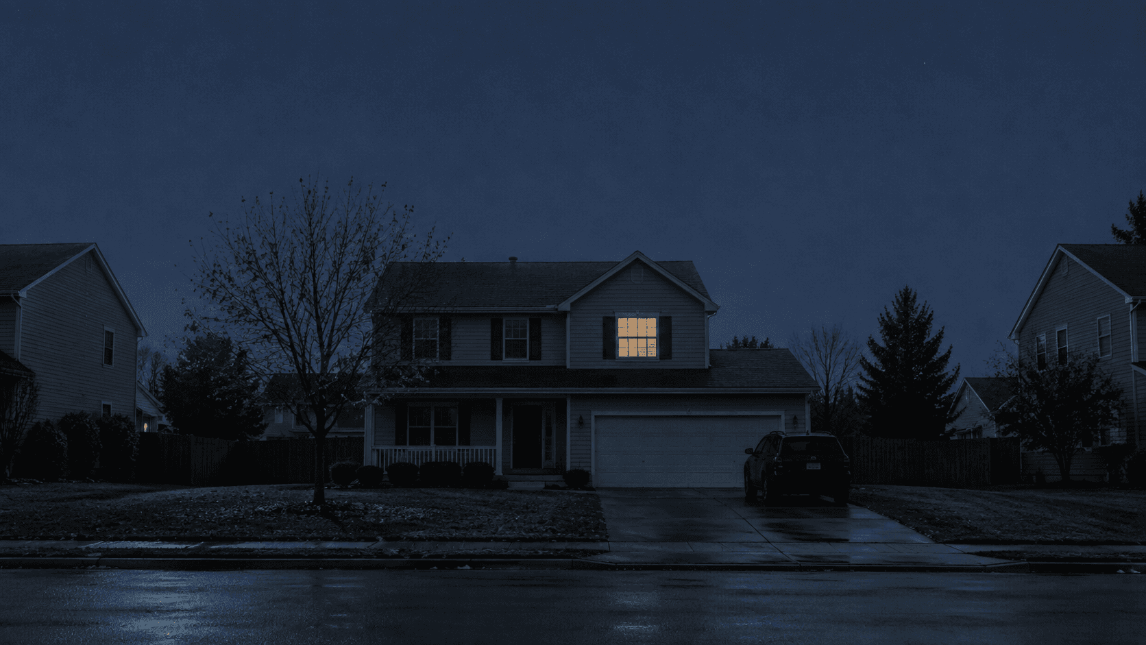 Two-story suburban house on a wet street at night with a single upstairs window lit, illustrating how psychological abuse looks ordinary from outside