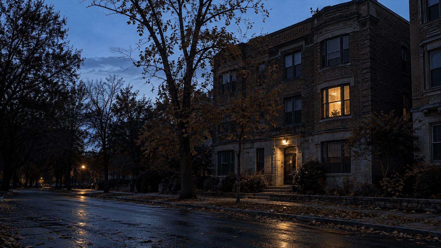 One apartment window glowing warmly above a dark street just before dawn